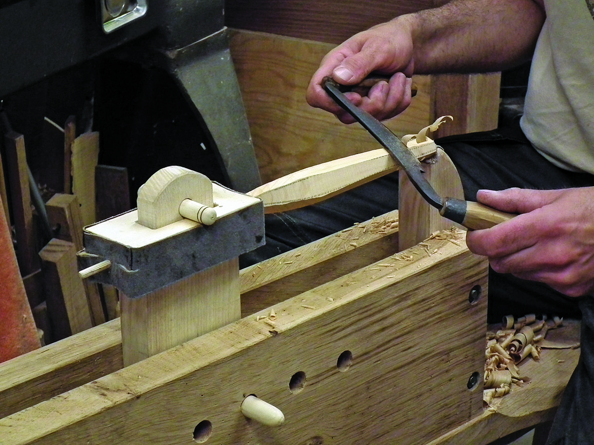 A small tool handle being worked in the shave horse with a drawknife.