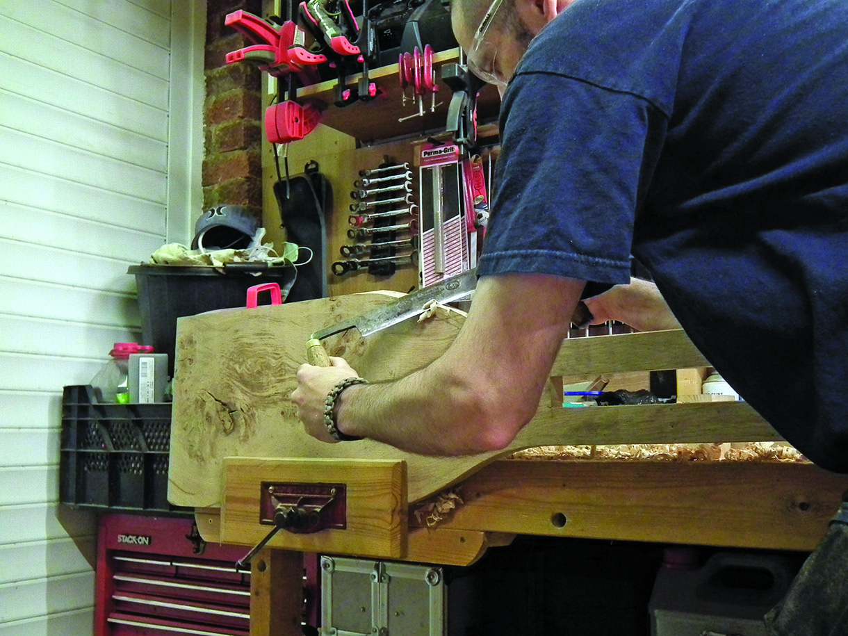Using a drawknife to chamfer the edge of the seat. The workpiece is held in a bench vice.