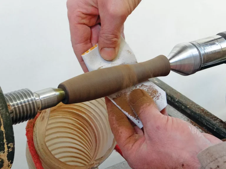 Woodturning on a lathe with hands sanding.