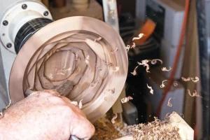 Woodturning on a lathe with wood shavings flying.
