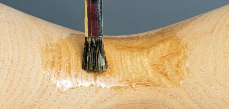 Brush applying varnish to wooden surface.