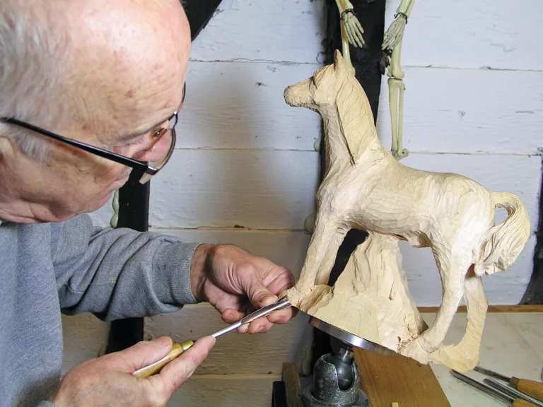 Man carving wooden horse sculpture.