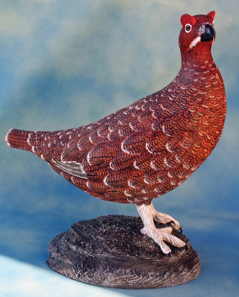 Red grouse bird statue on a rock base.