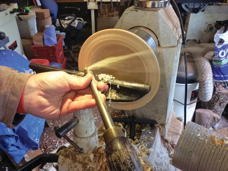 Woodturning on lathe with hand tool.