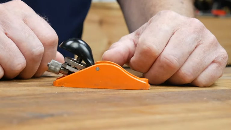 Using an orange woodworking hand plane tool on table.