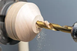 Drill bit cutting into spinning wood on lathe.