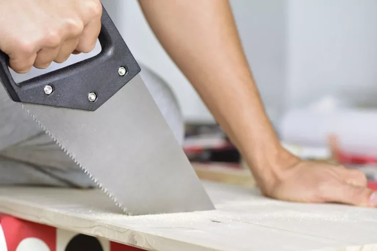 Carpenter sawing wood with a hand saw.