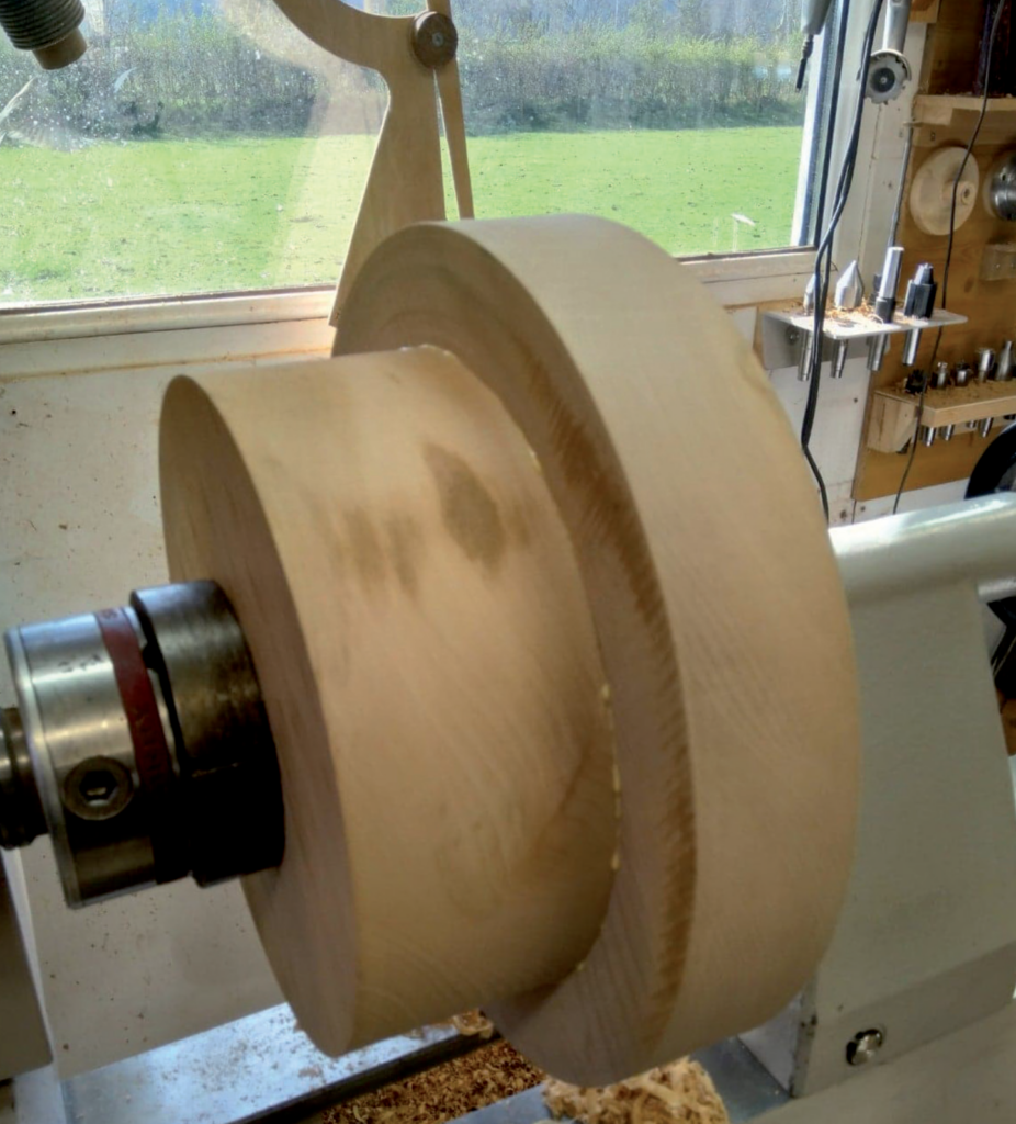Wood lathe in action, carving a large wooden bowl.