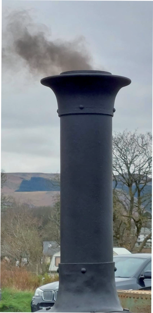 Black chimney emitting smoke in a rural setting.
