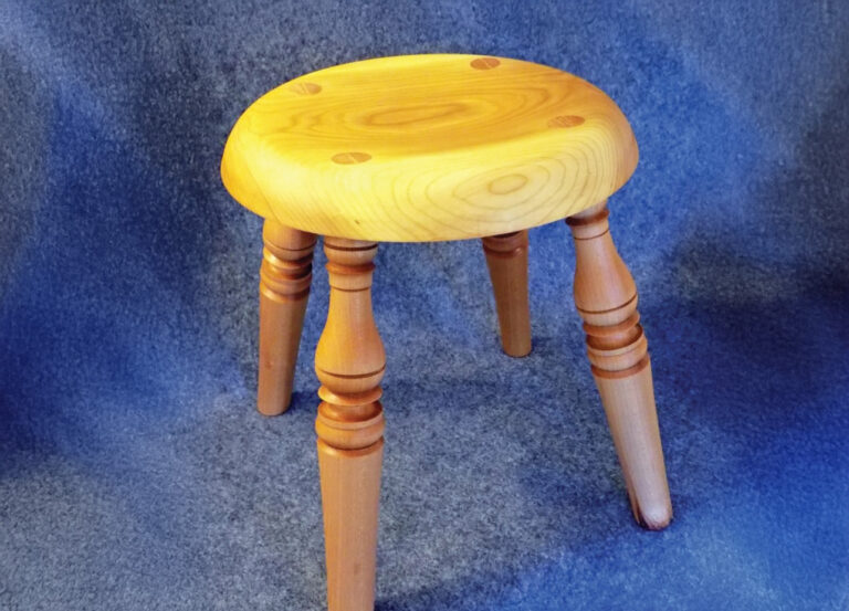 Wooden three-legged stool on blue surface.