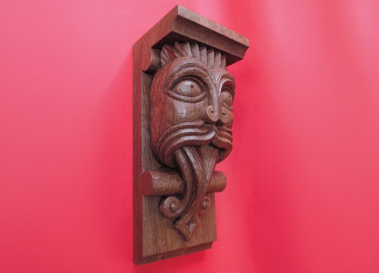 Wooden gargoyle carving on red background.