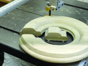 Bandsaw carving wooden car inside ring on table.