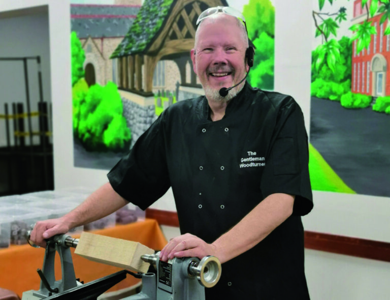 Man demonstrating woodturning on lathe, smiling.