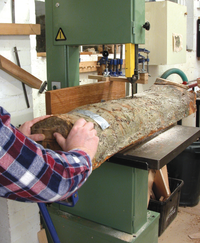 Person sawing log with bandsaw in workshop
