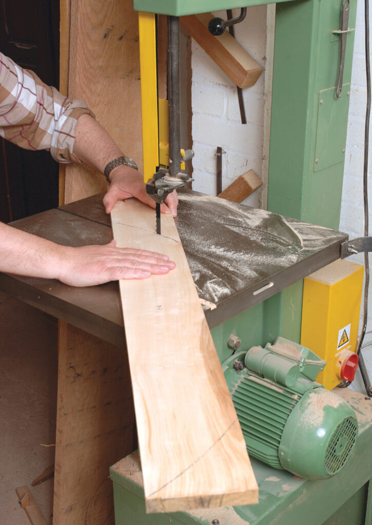 Person using bandsaw to cut wood plank.