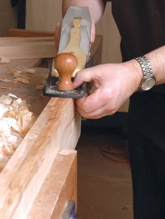 Person planing wood with a hand tool, workshop context.