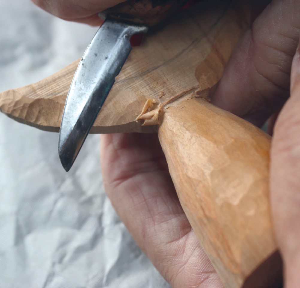 Close-up of hand carving wood with knife.