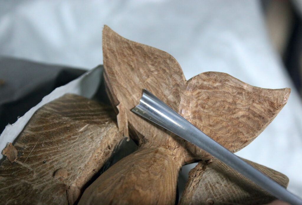 Chisel carving intricate wooden flower design.