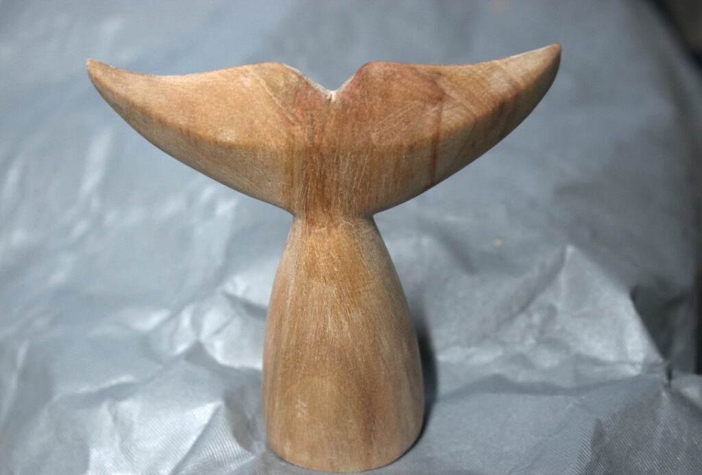 Wooden whale tail sculpture on grey background