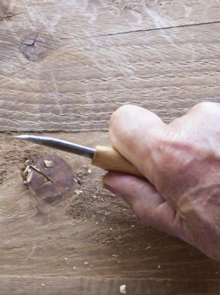 Hand carving wood with a chisel tool.