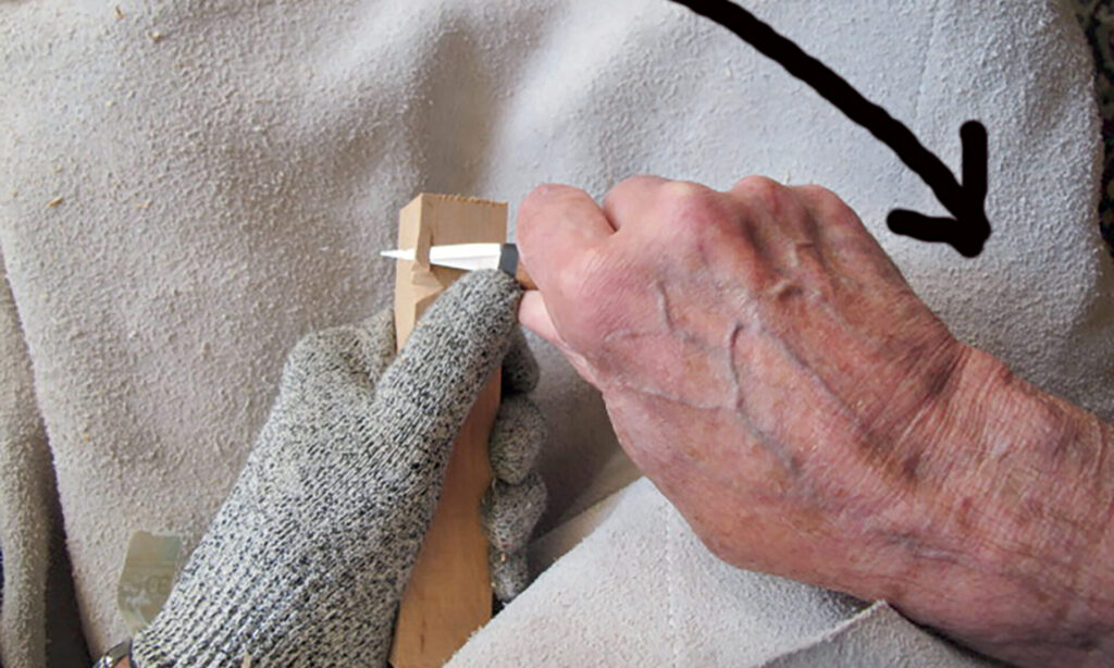 Person carving wood with gloved hand.