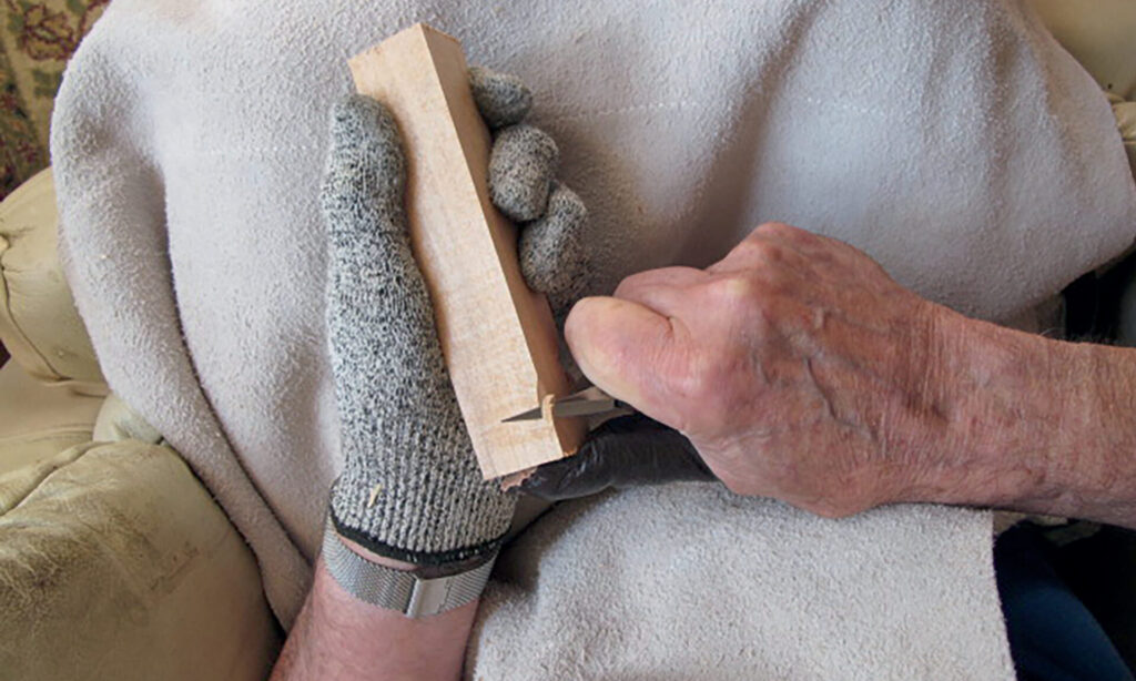 Person carving wood with a glove and knife.