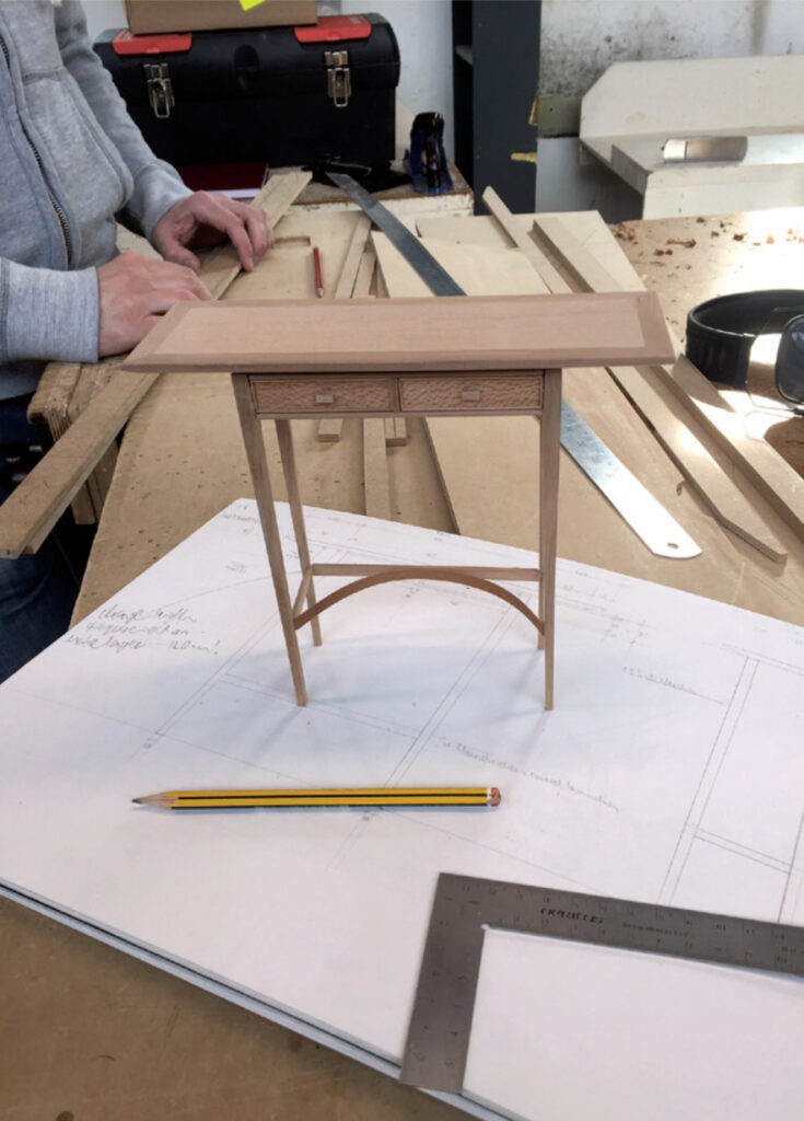 Model wooden desk on design plans in workshop.
