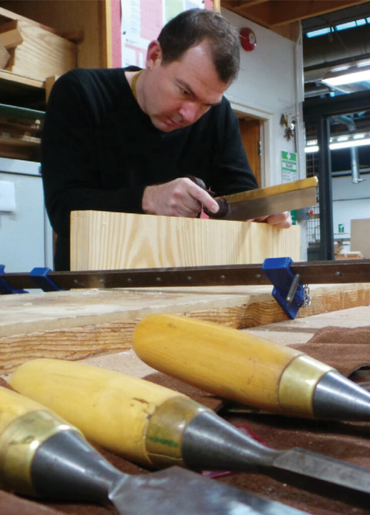 Man woodworking with saw in workshop setting.