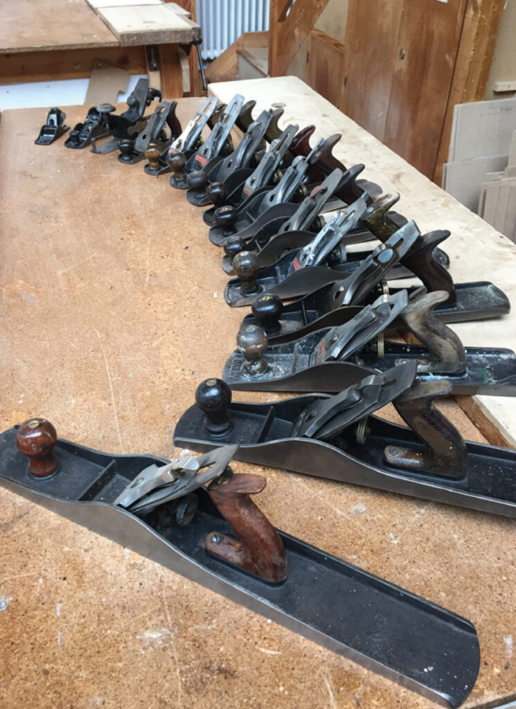 Row of vintage woodworking planes on workshop table.