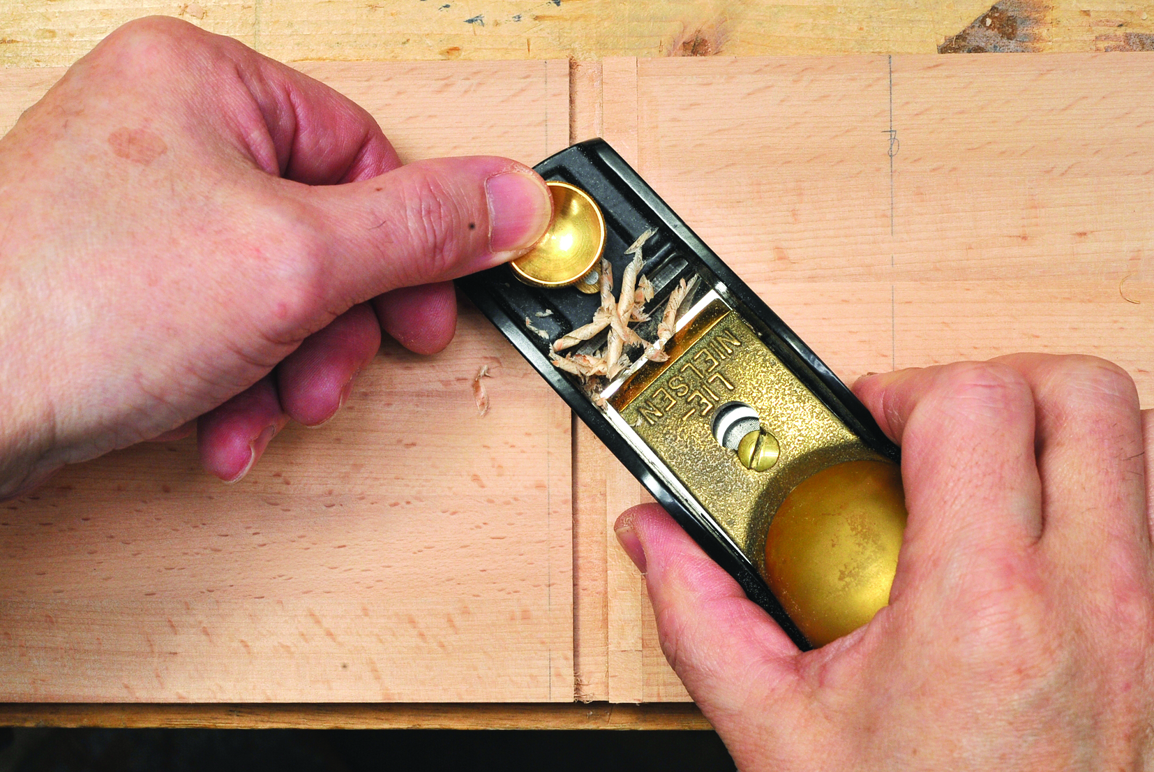 Using hand plane to smooth wooden surface.