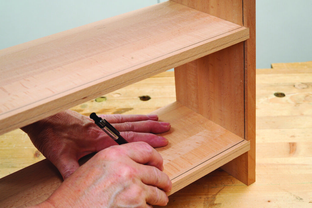 Craftsman measures wooden shelf with pencil.