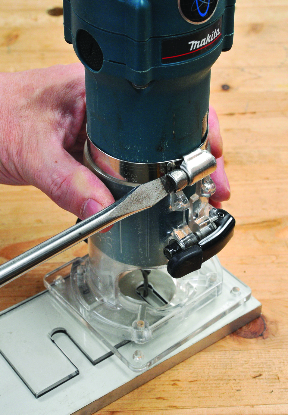 Person adjusting router tool on wooden table.