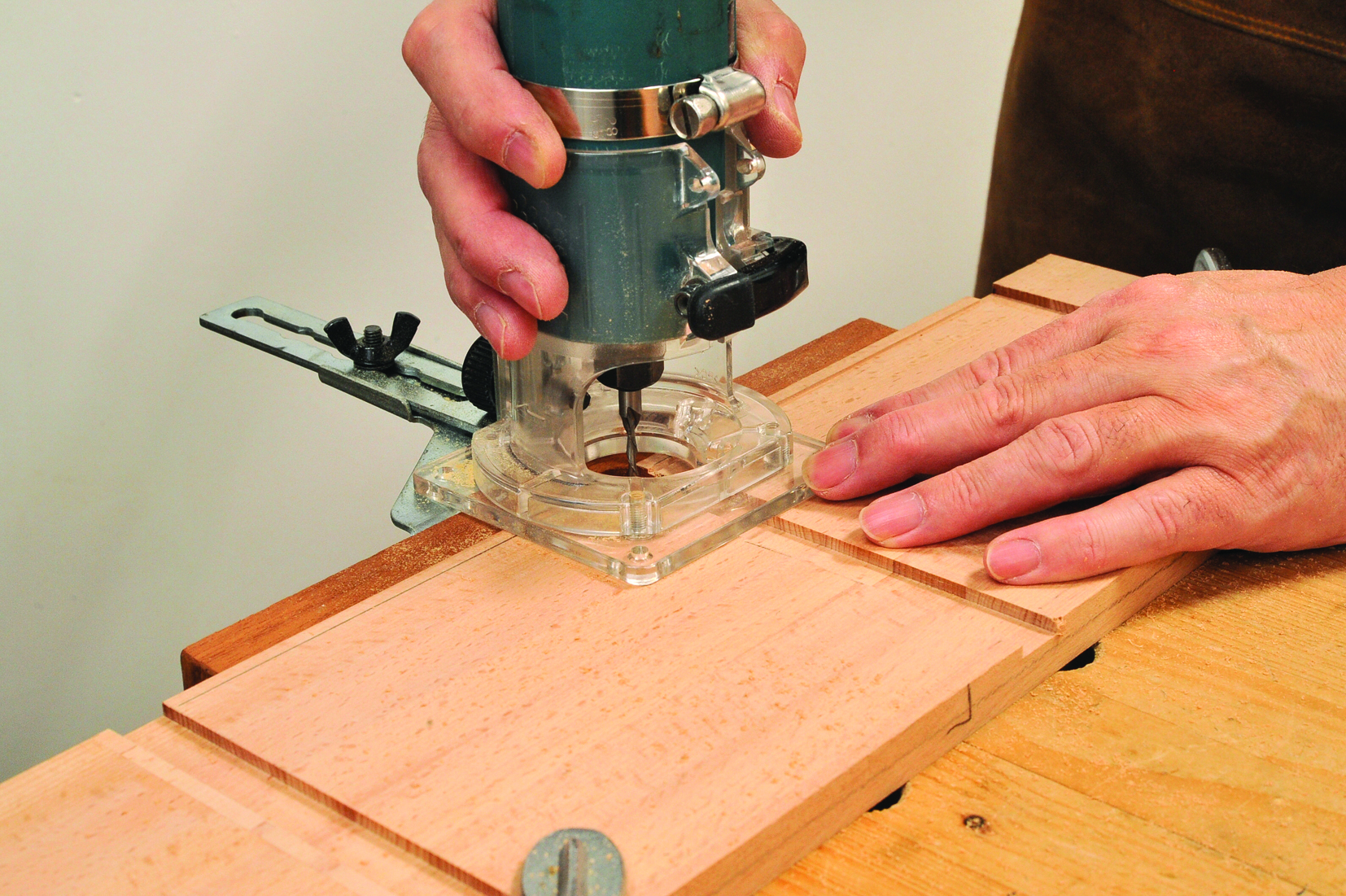 Person using hand router on wooden plank.