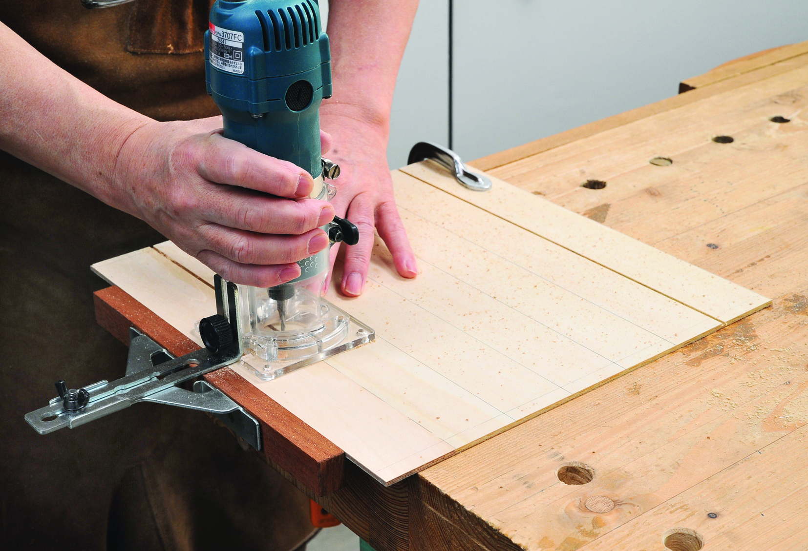 Person using electric router on wooden board.