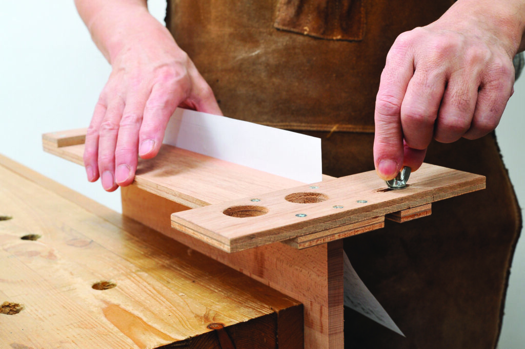 Person adjusting wooden jig with white paper.