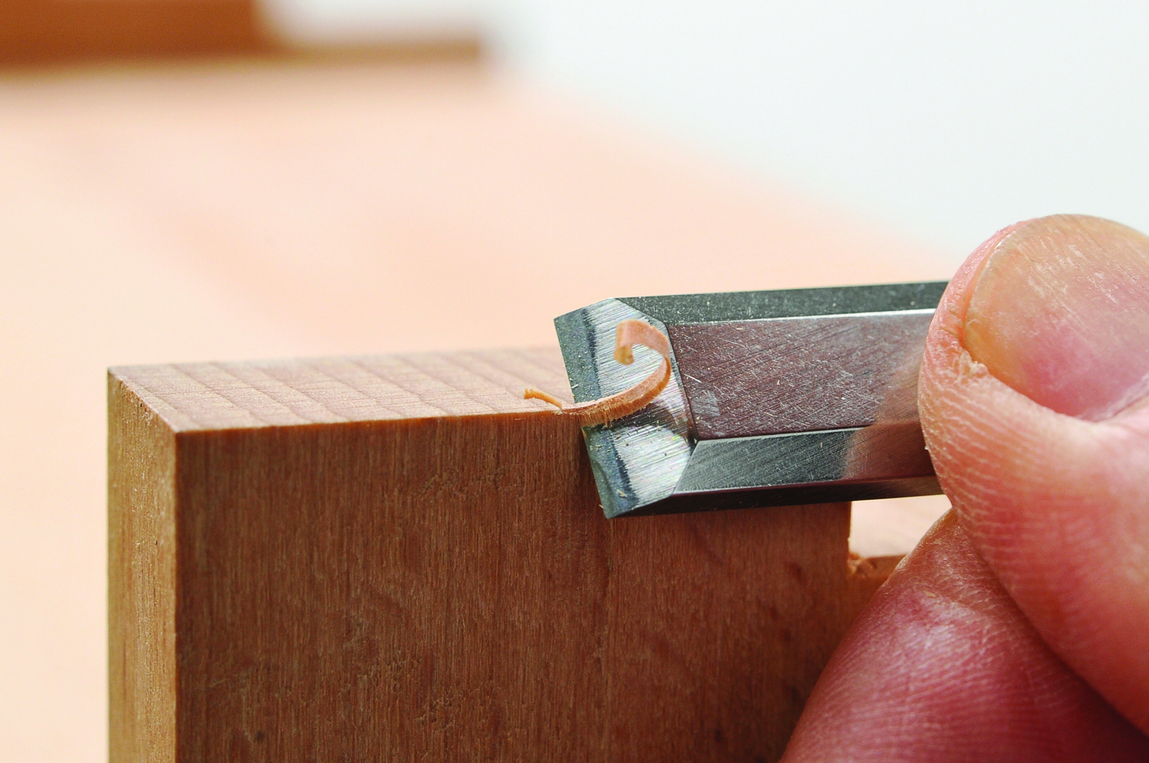Hand using chisel to carve wood edge.