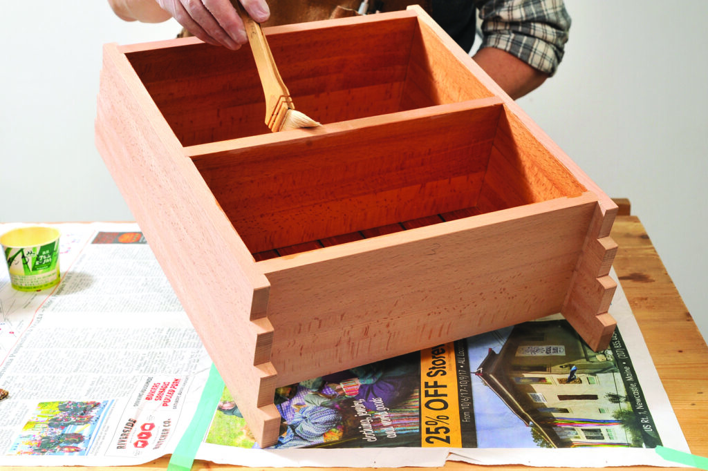 Person varnishing wooden box on table.