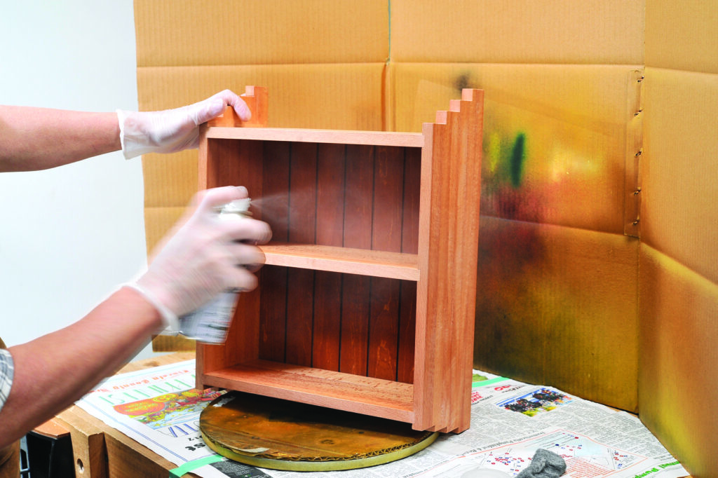 Person spray painting wooden shelf in workshop.