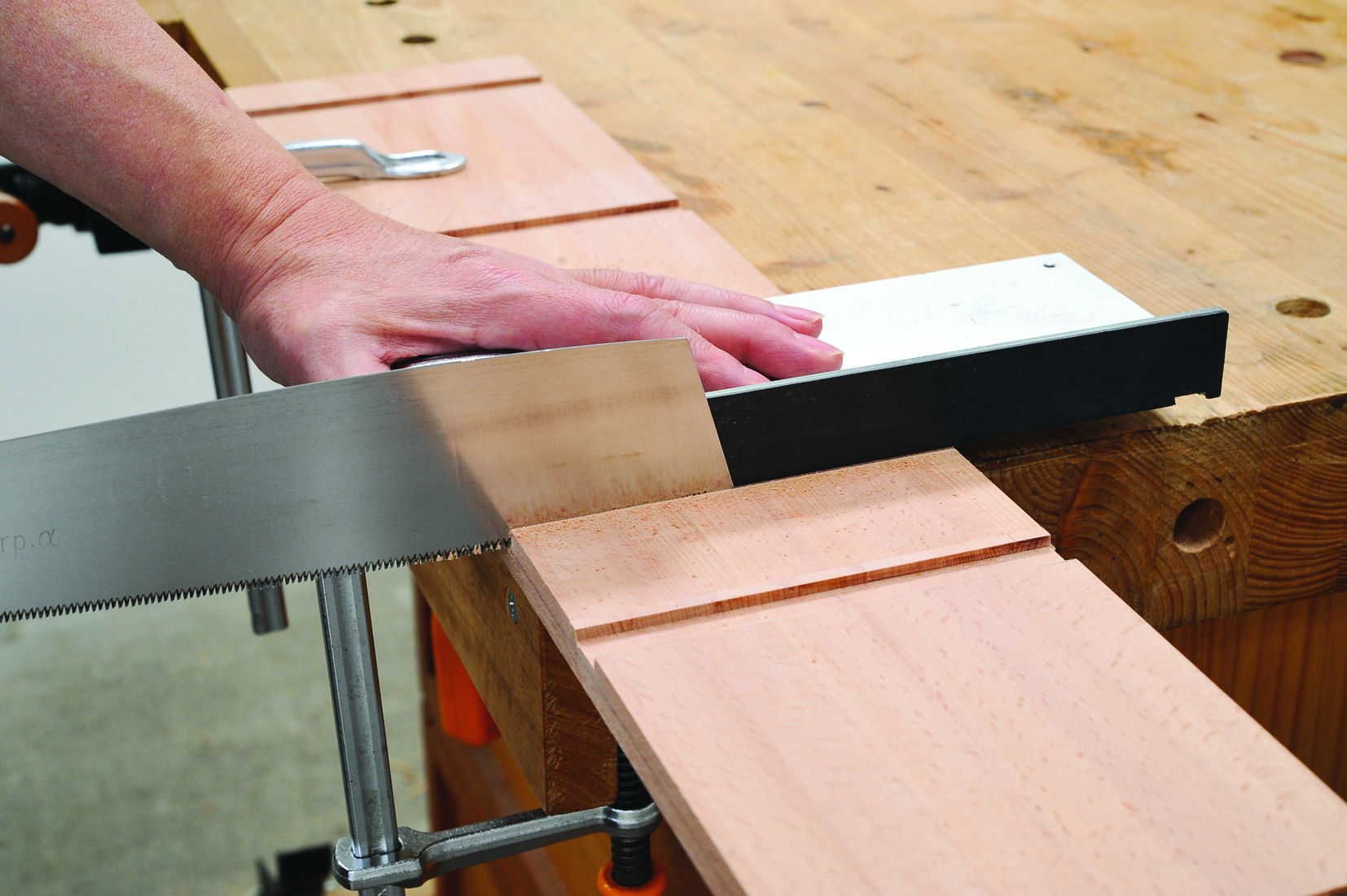 Hand using saw to cut wood on workbench