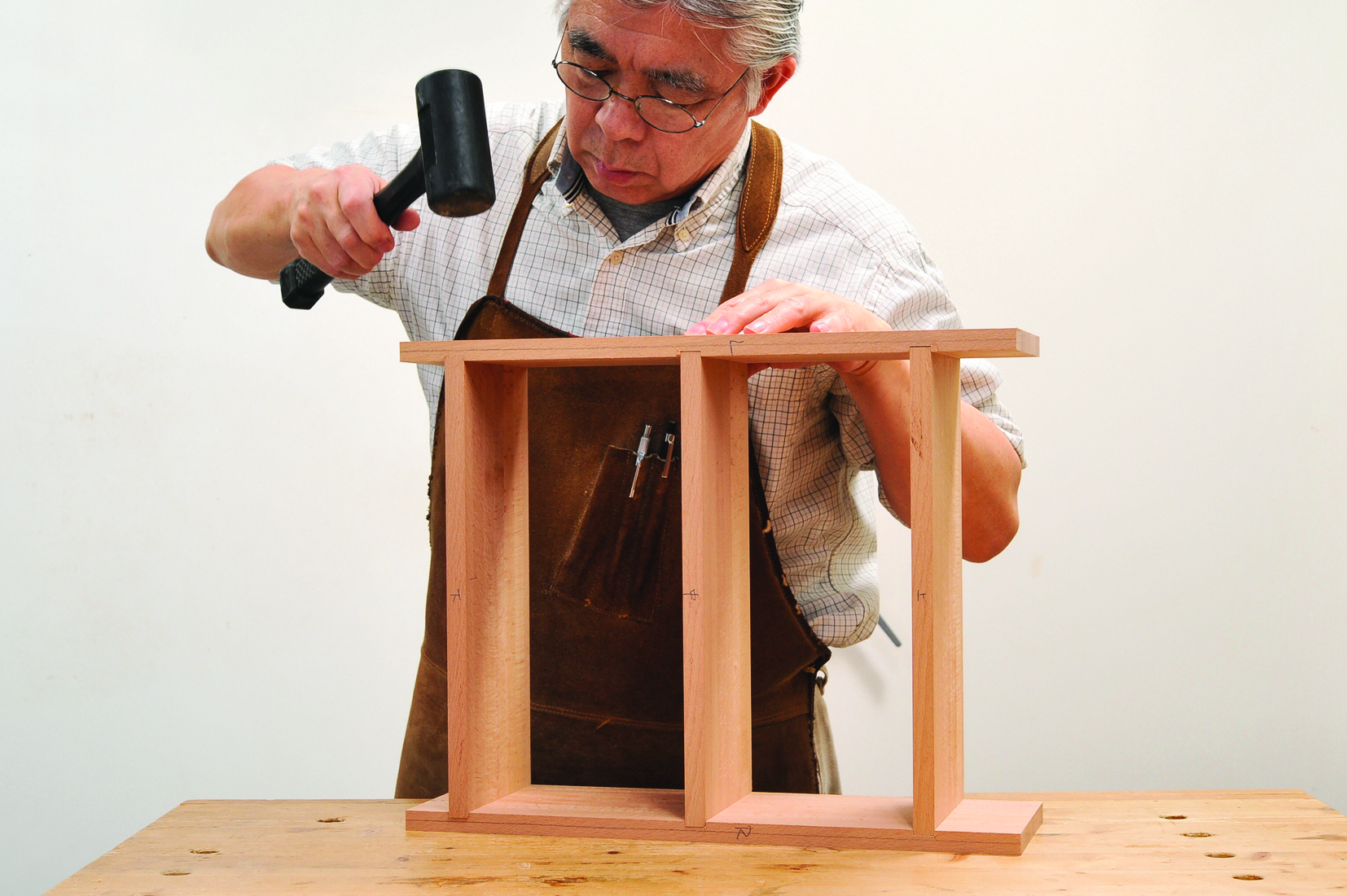 Carpenter assembling wooden shelf with mallet.