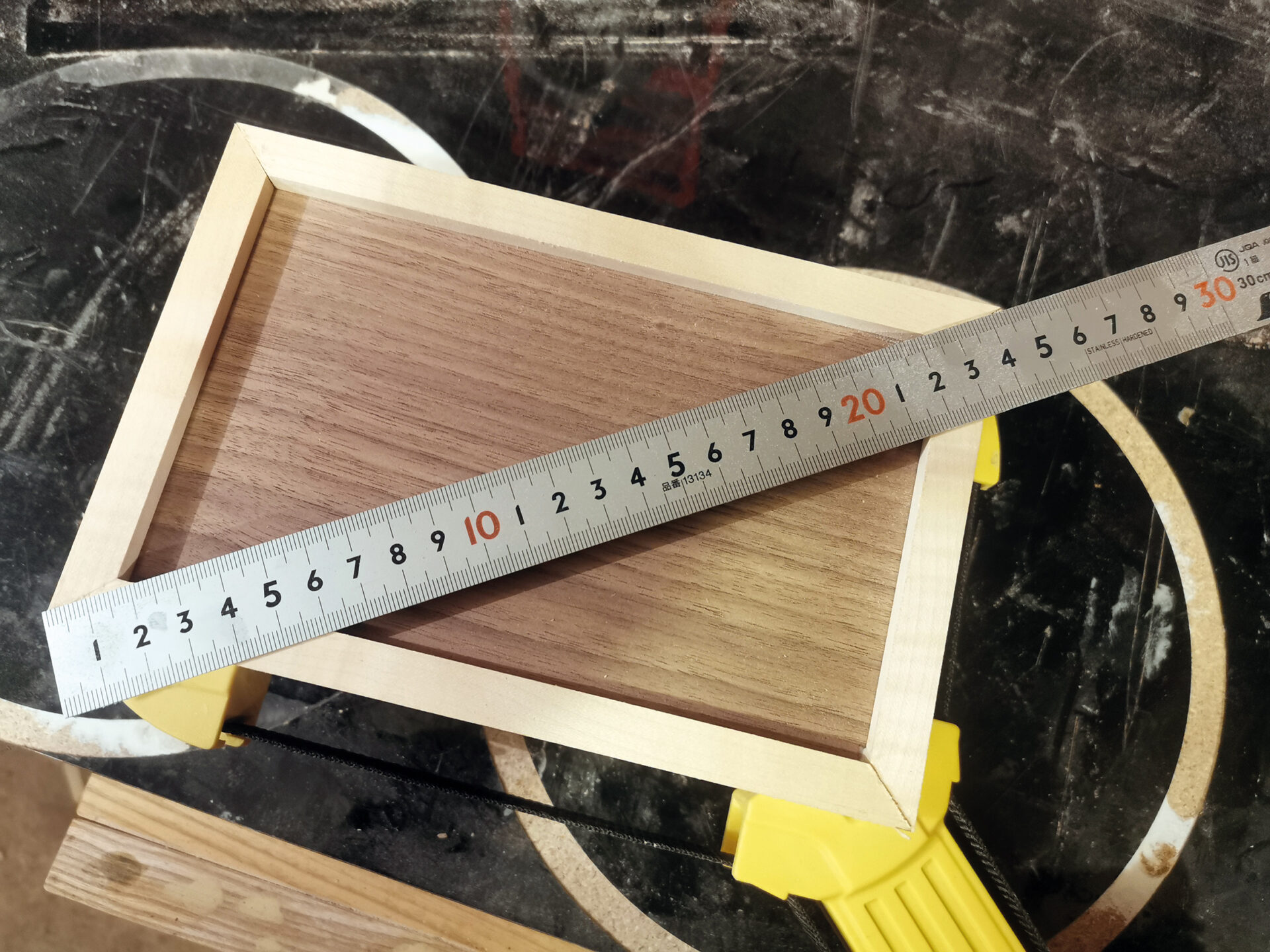 Measuring wooden frame with metal ruler on table.