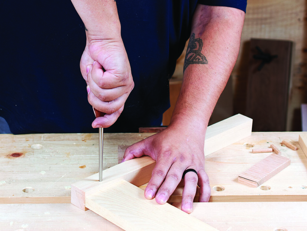 Carpenter chiselling wood on workbench.