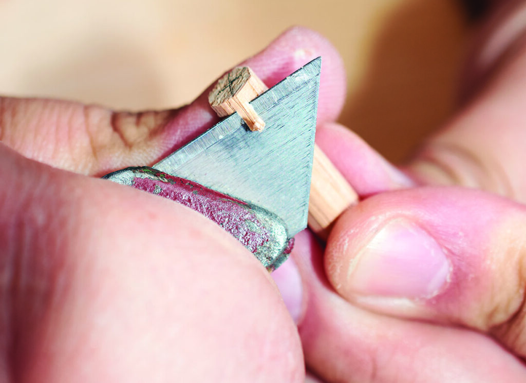 Carving small wooden peg with precision knife.