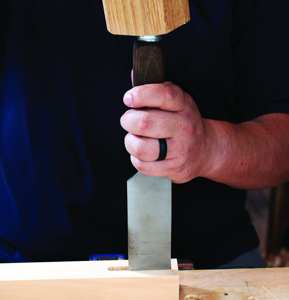 Woodworker using chisel and mallet on wood piece.