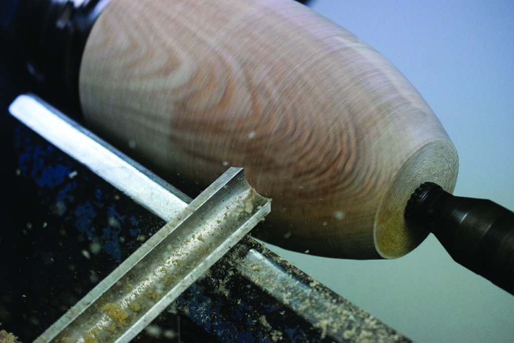 Woodturning with chisel on lathe, close-up view.