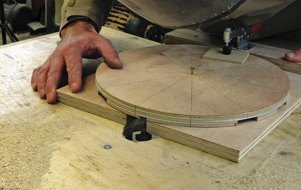 Woodworker using router on circular plywood piece.