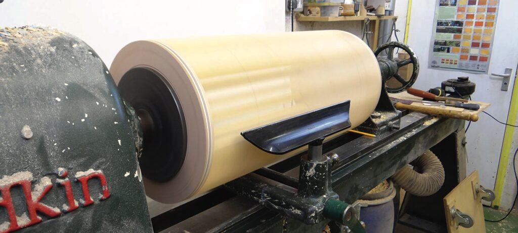 Large wood lathe shaping cylinder in workshop.