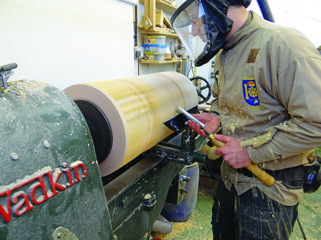 Woodturner shaping wood piece on lathe machine.