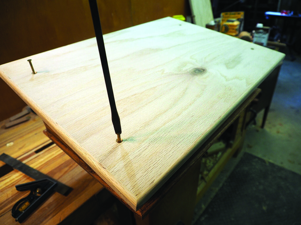 Drilling screws into wooden board on workbench.