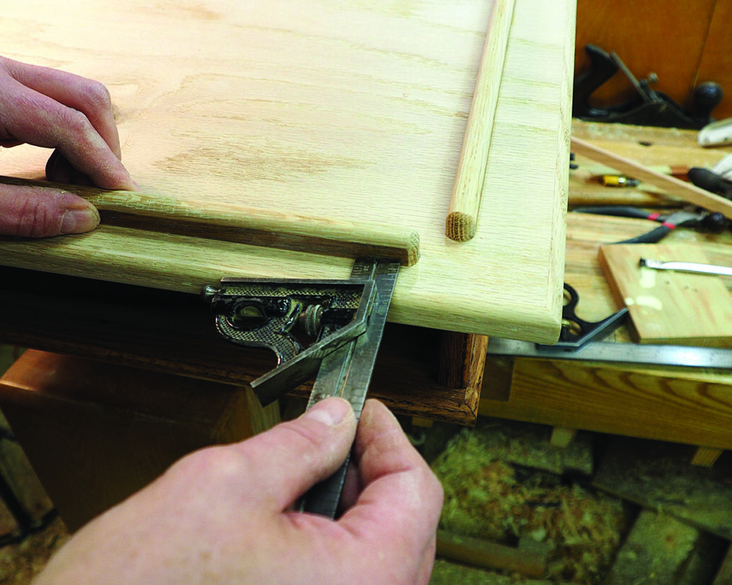 Craftsperson measuring wooden board with square tool.